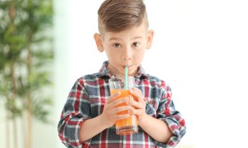 Enfant qui boit un jus de fruits, une boisson nocive pour la santé buccodentaire.